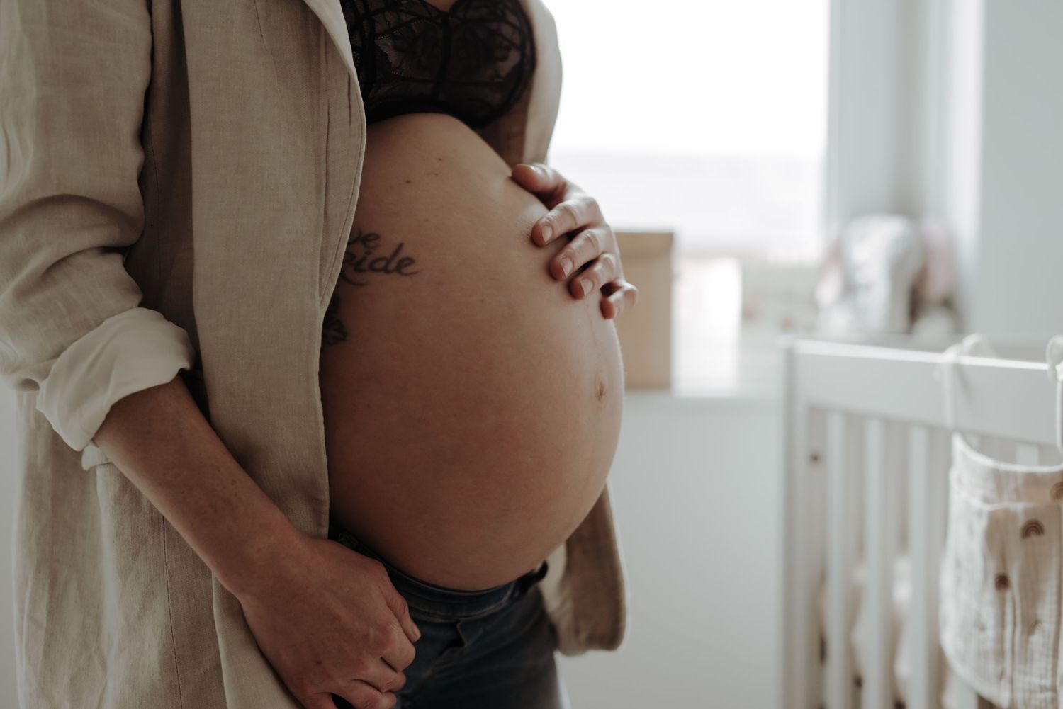 Close-up of a pregnant belly being gently cradled by hands in soft natural lighting.
