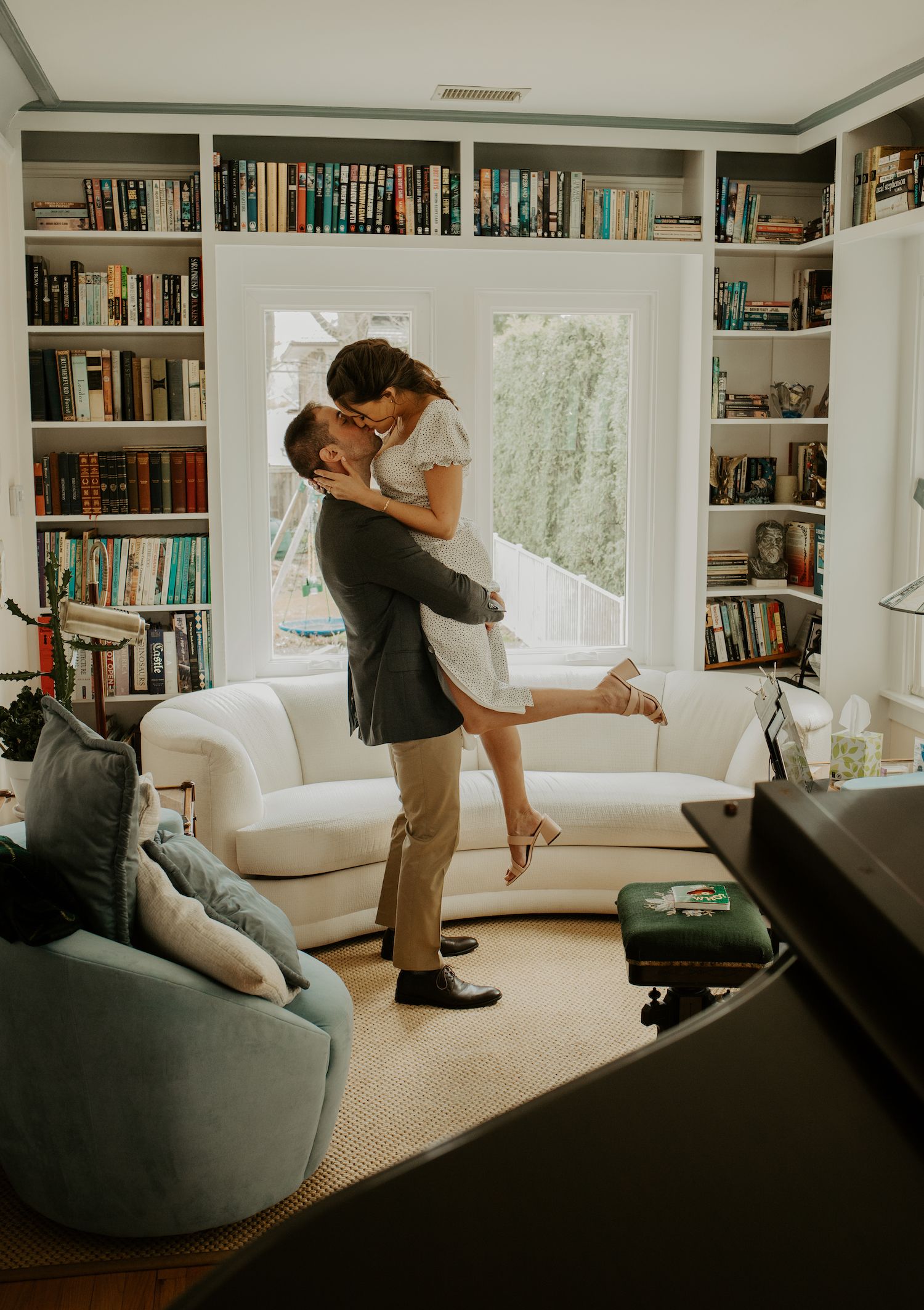 A playful lifting pose in a modern living room surrounded by built-in bookshelves.