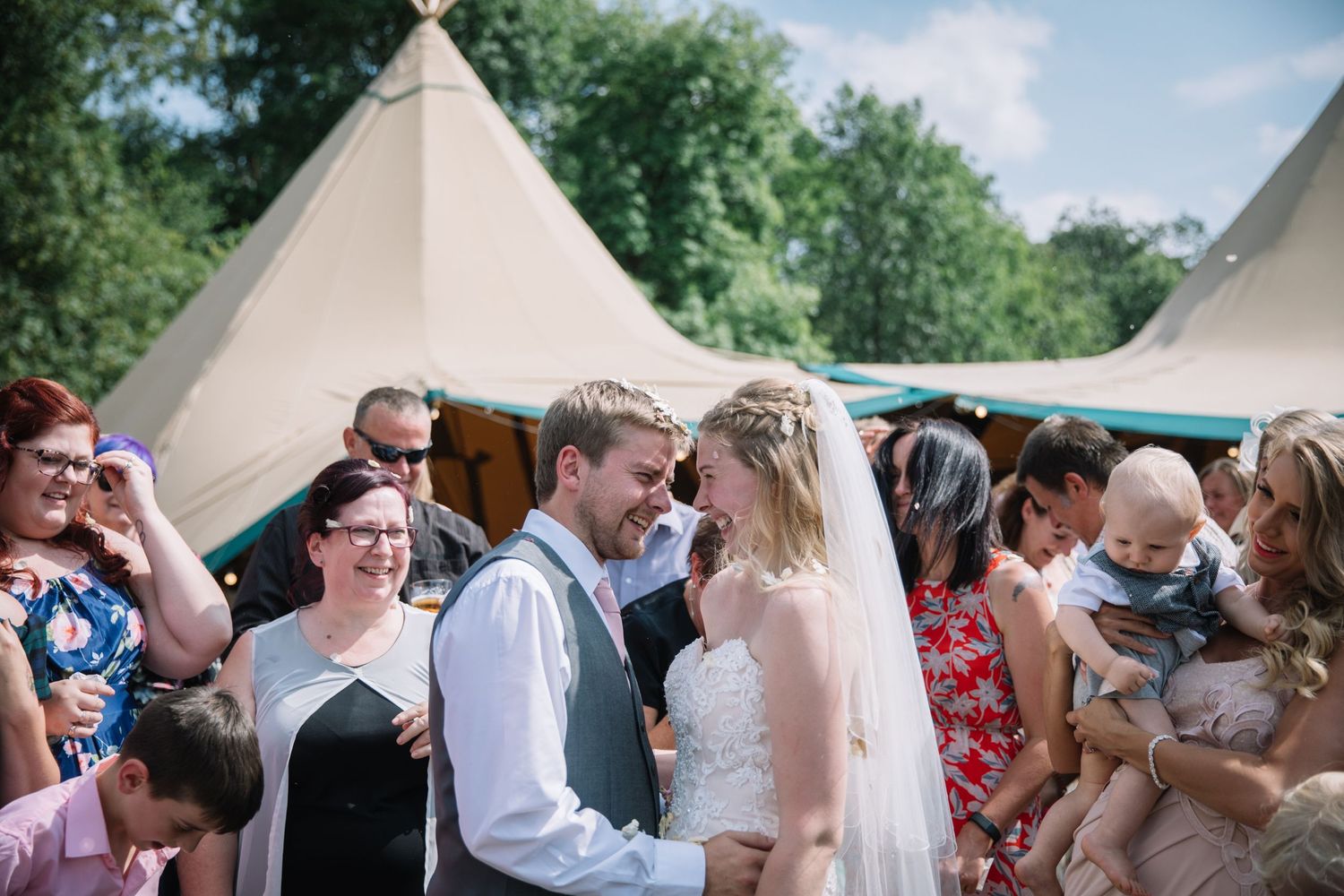 A wedding ceremony taking place outside with white teepee tents and guests watching.