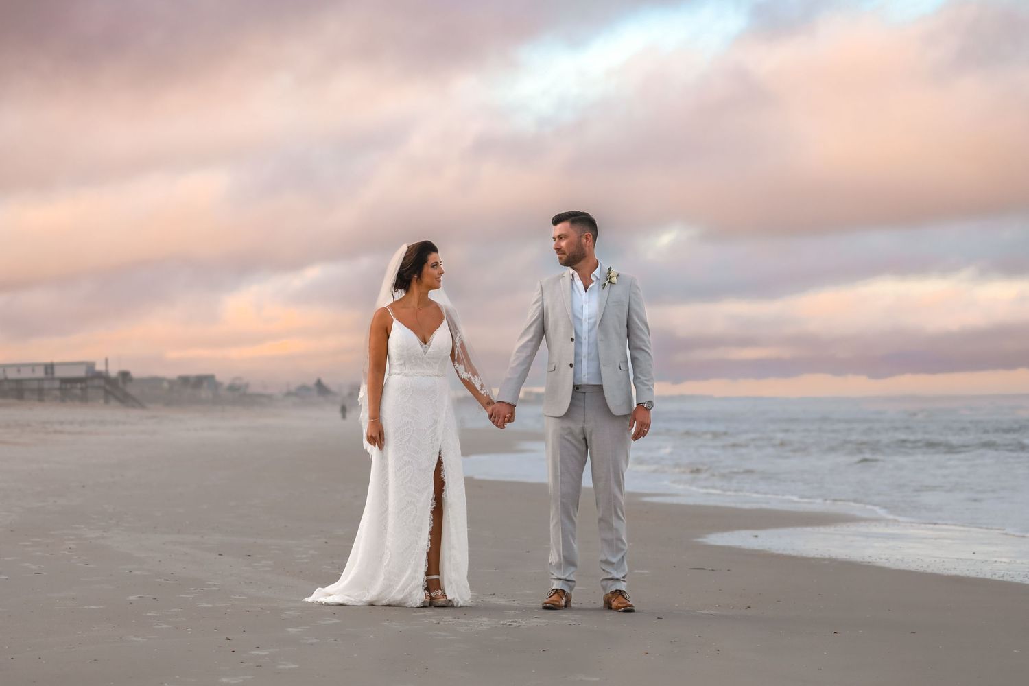 Romantic beach wedding portrait at sunset with couple holding hands.