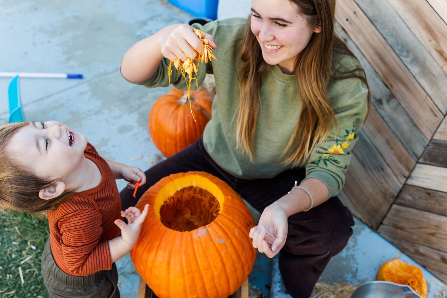 People scooping out seeds from a large orange pumpkin during fall harvest activities.