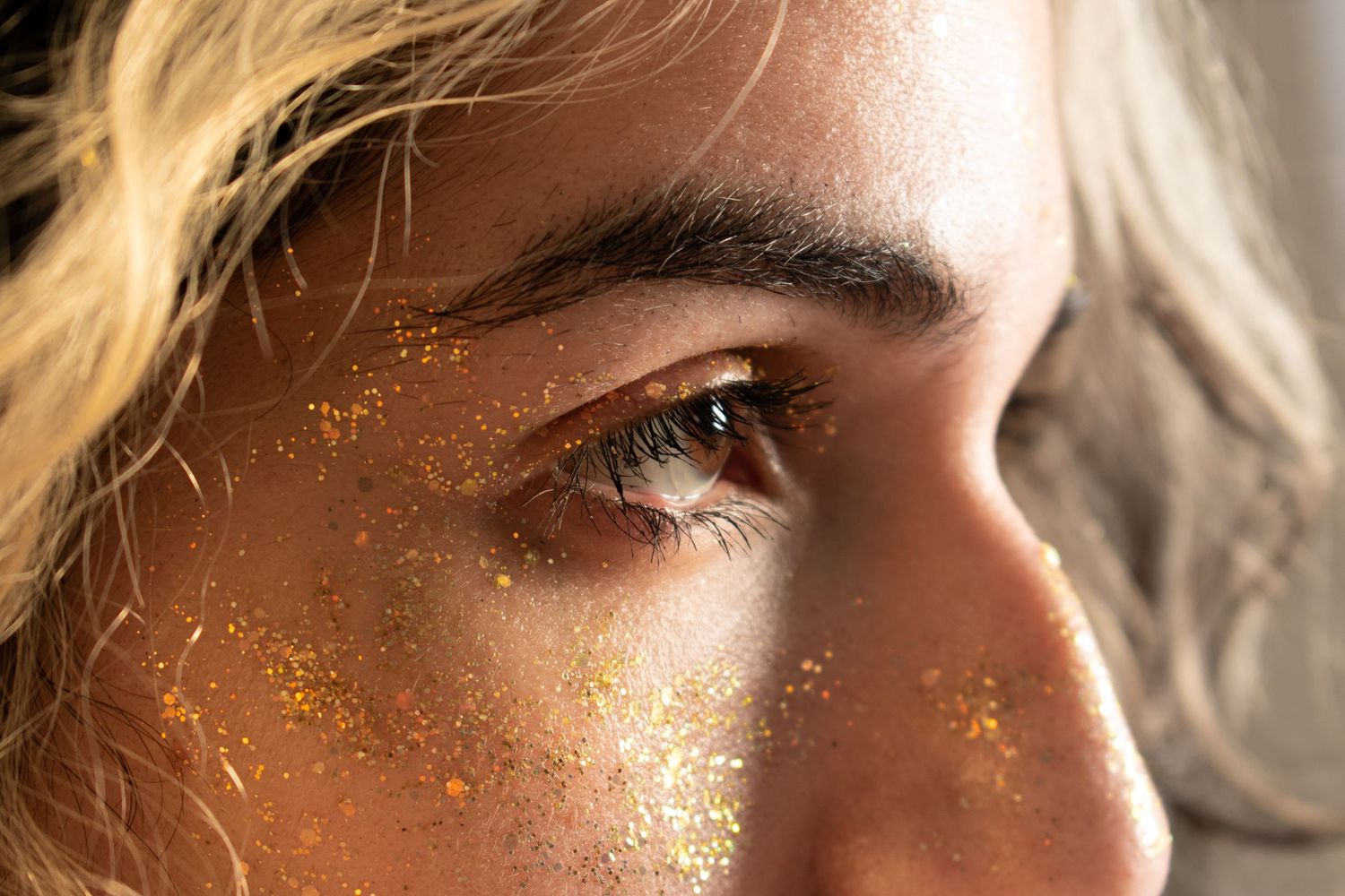 Close up profile shot showing glittery gold makeup sparkles on face in warm lighting.