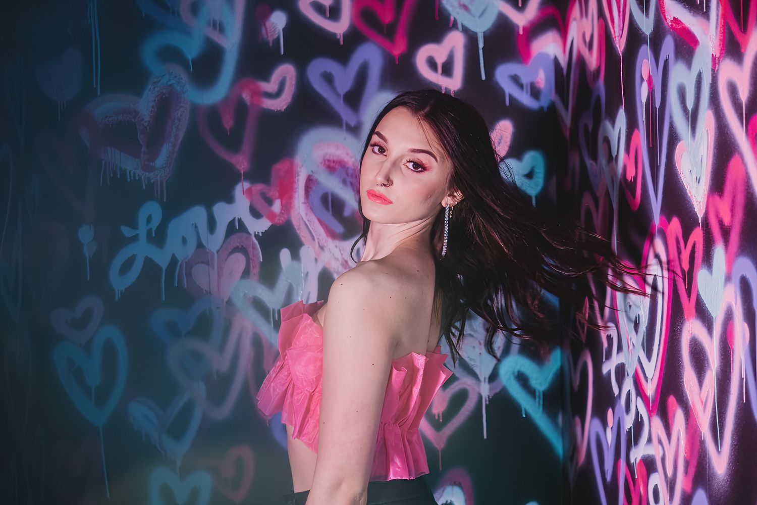 Fashion portrait against neon heart graffiti wall with pink and blue lighting.