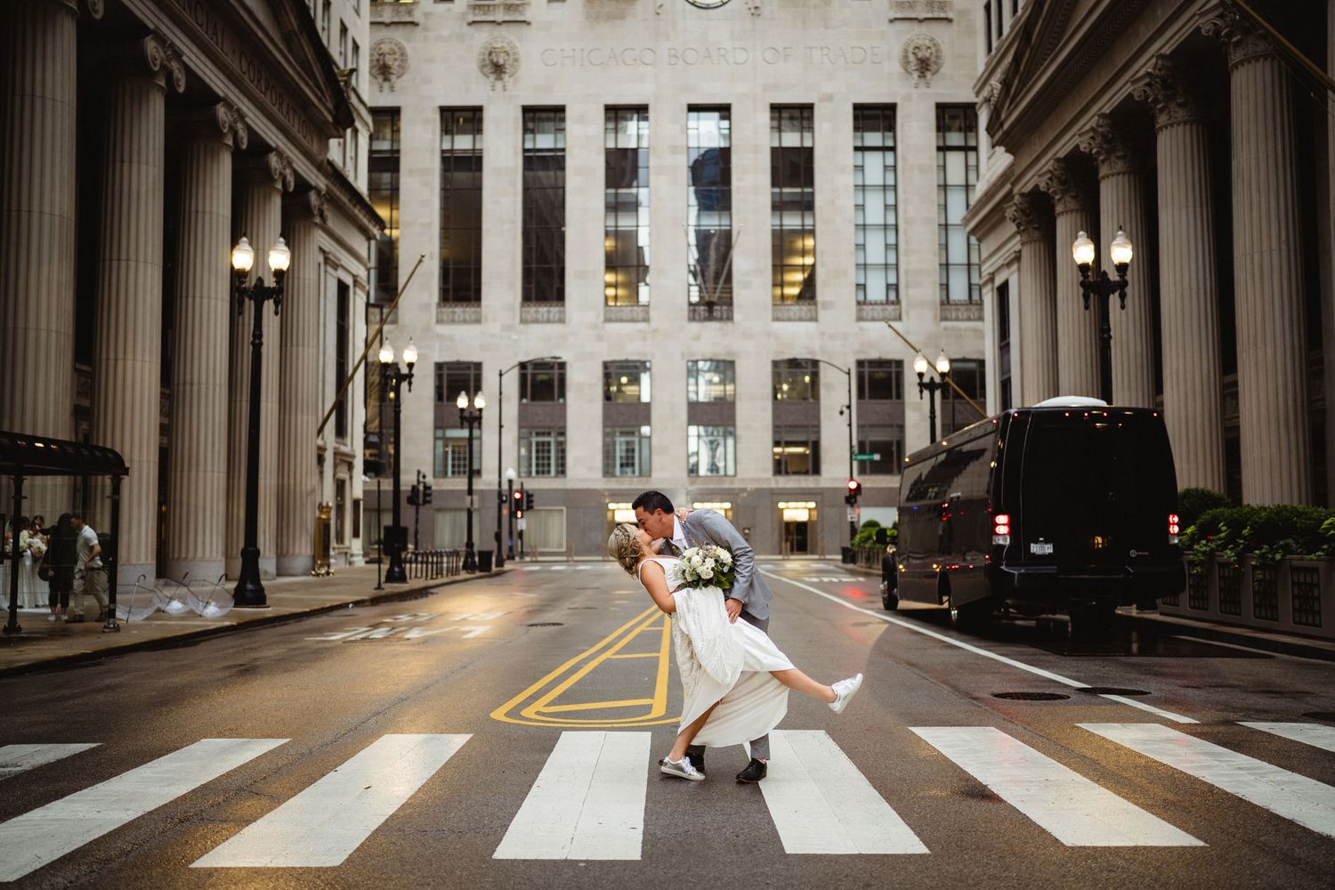 A couple shares a romantic dip pose on a crosswalk between classic stone columns in an urban setting.