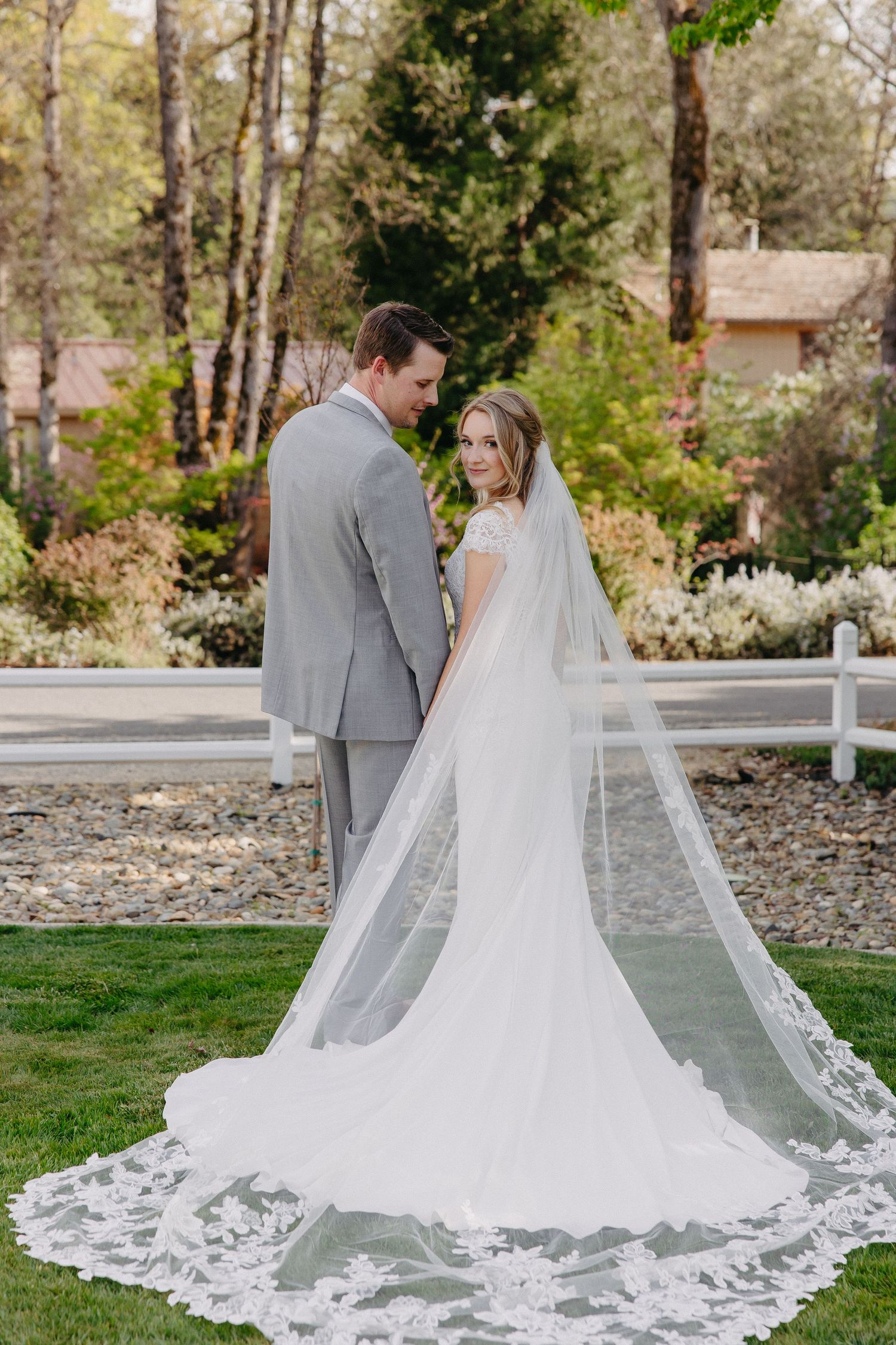 Wedding couple stands together showing detailed lace train of bride's gown.