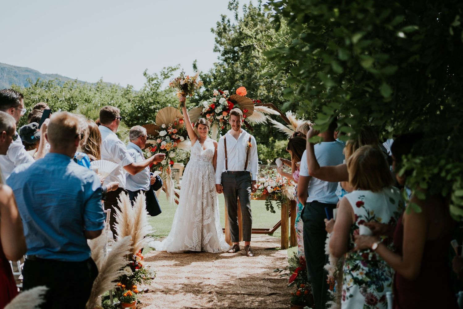 A wedding ceremony in a garden pathway with guests lining both sides.