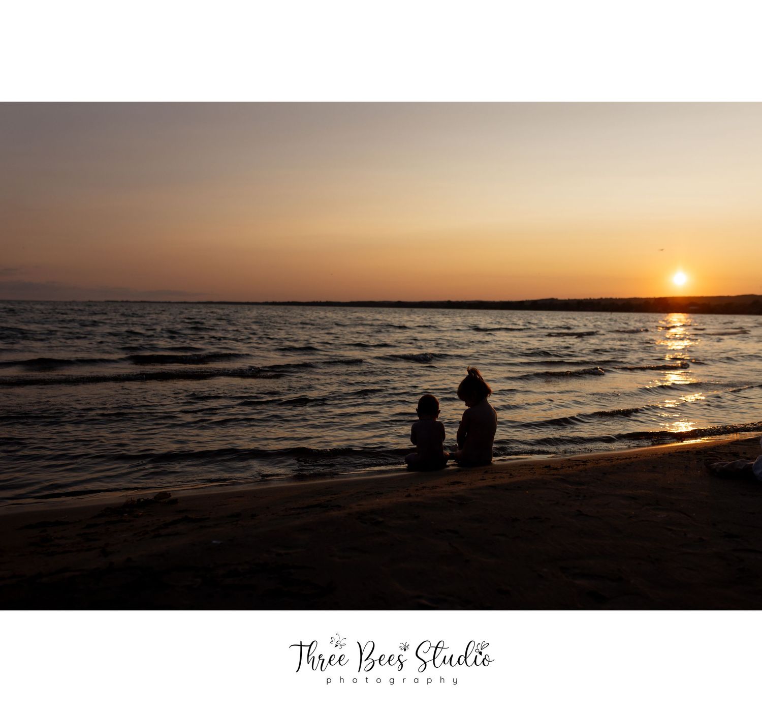 Silhouettes on beach watching sunset over ocean horizon.
