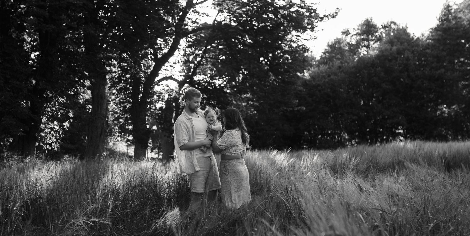 Vintage black and white photograph showing three people standing together in a grassy meadow with trees in background.
