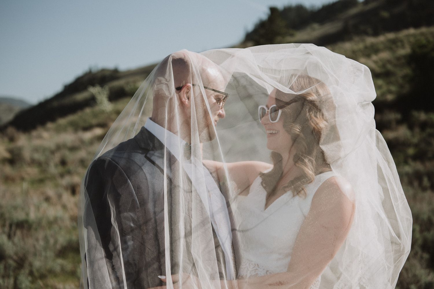 Bride and Groom wedding photos. Bride and groom are facing each other smiling, while the brides veil covers them. Oliver