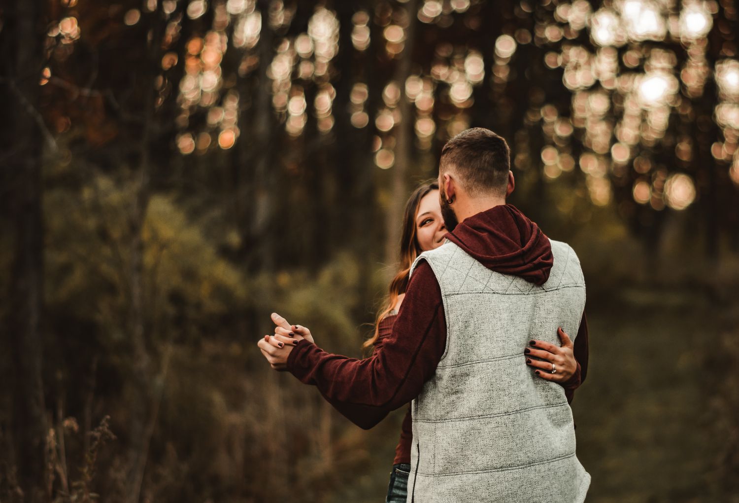 Romantic autumn engagement photo of couple embracing in golden sunset light.