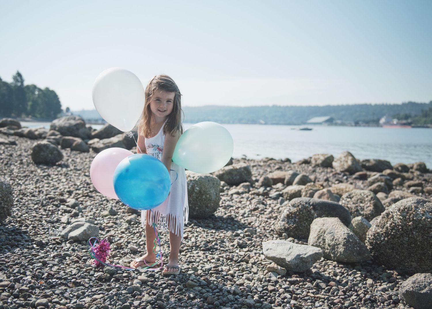 A peaceful moment on a rocky beach with white and blue balloons floating in the sea breeze.