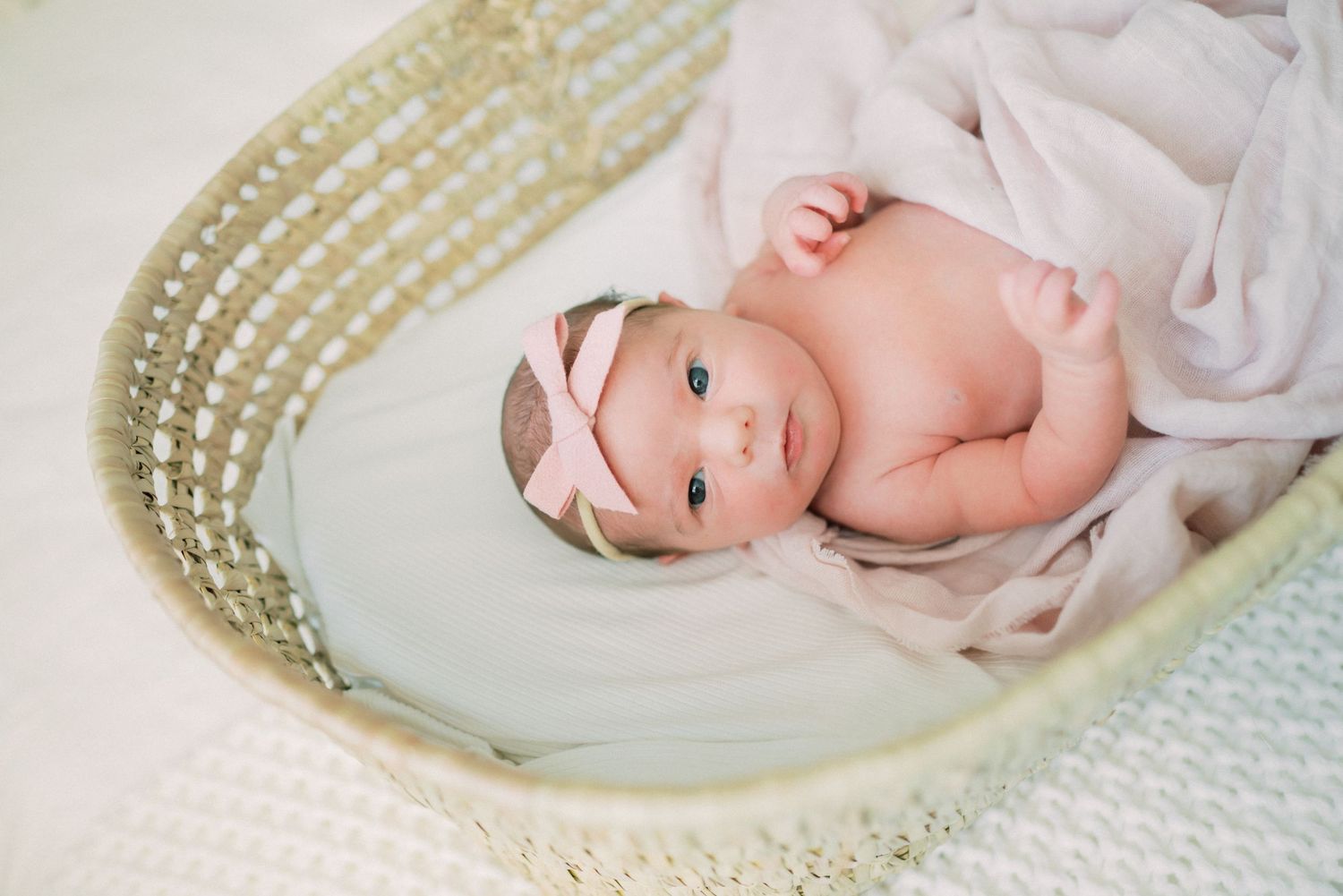 Newborn baby wrapped in white fabric lying in woven basket with delicate pearl details.