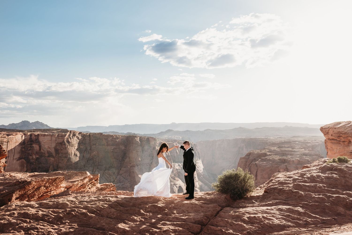 Panoramic view of red rock cliffs and desert landscape under cloudy skies at sunset.