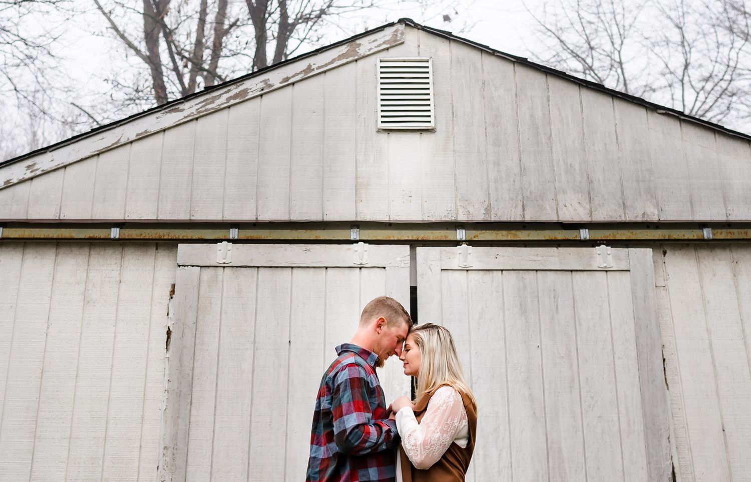 A couple shares tender moments against a rustic white barn wall.