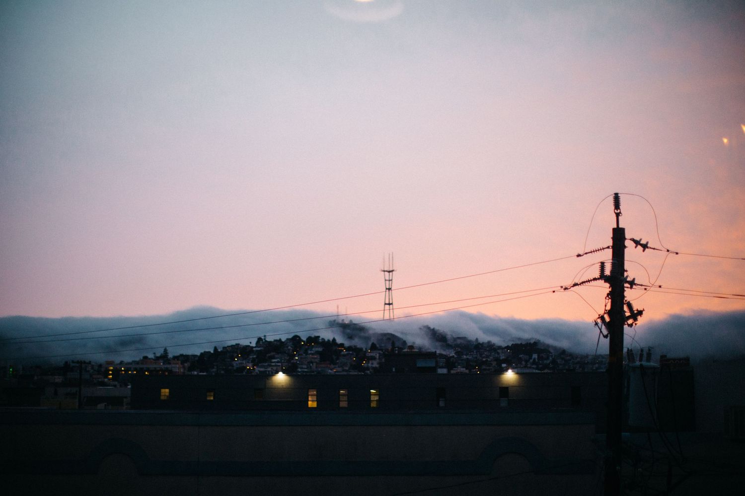 A stunning sunset view of a hillside town with silhouetted power lines against a pink sky.