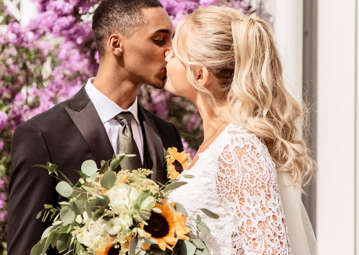 A couple shares a romantic moment with sunflowers among purple flowers.
