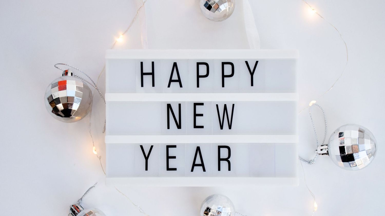 Happy New Year lightbox sign with silver disco balls and string lights.