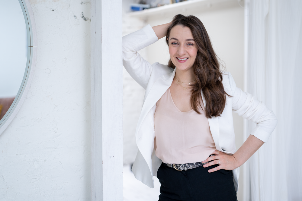 Fashion portrait featuring white blazer and dark pants in bright interior setting.