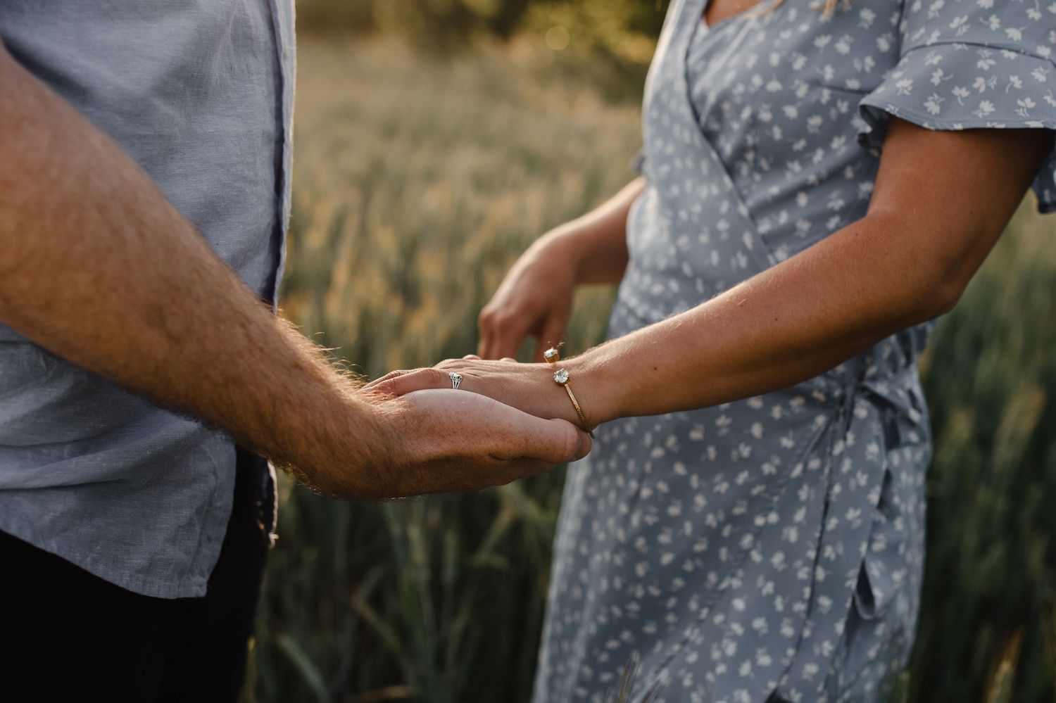 Close-up of hands holding each other tenderly in evening sunlight.