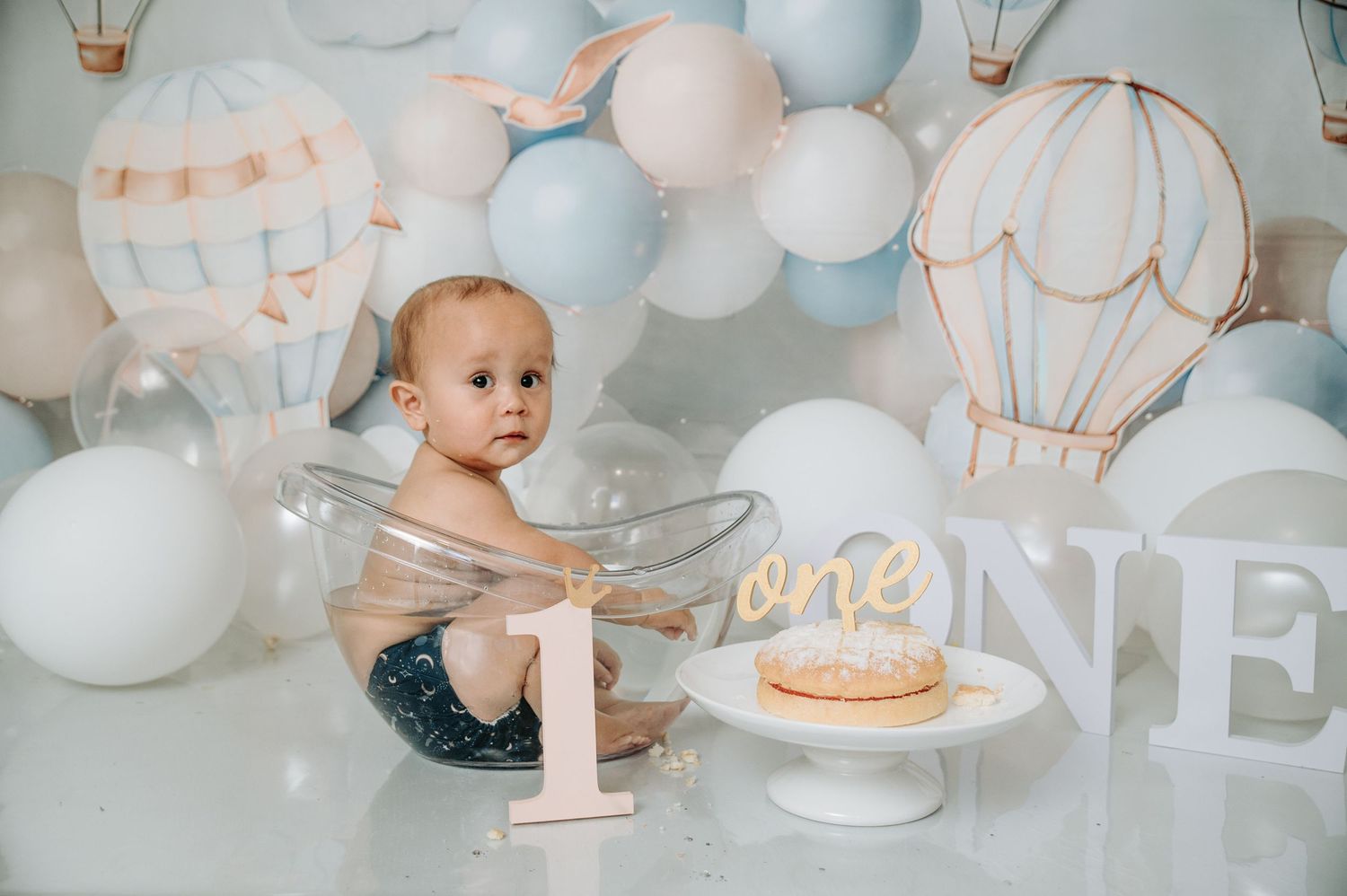 Baby in clear bowl with hot air balloon themed first birthday setup.