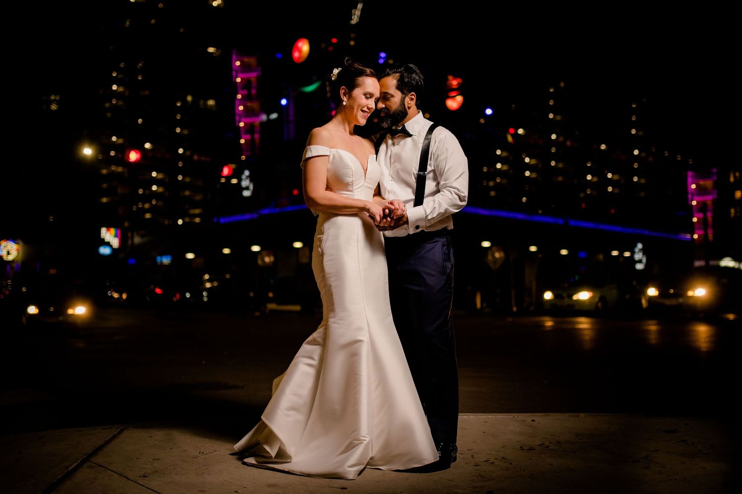 A couple shares a romantic moment dancing at night with city lights glowing in the background.