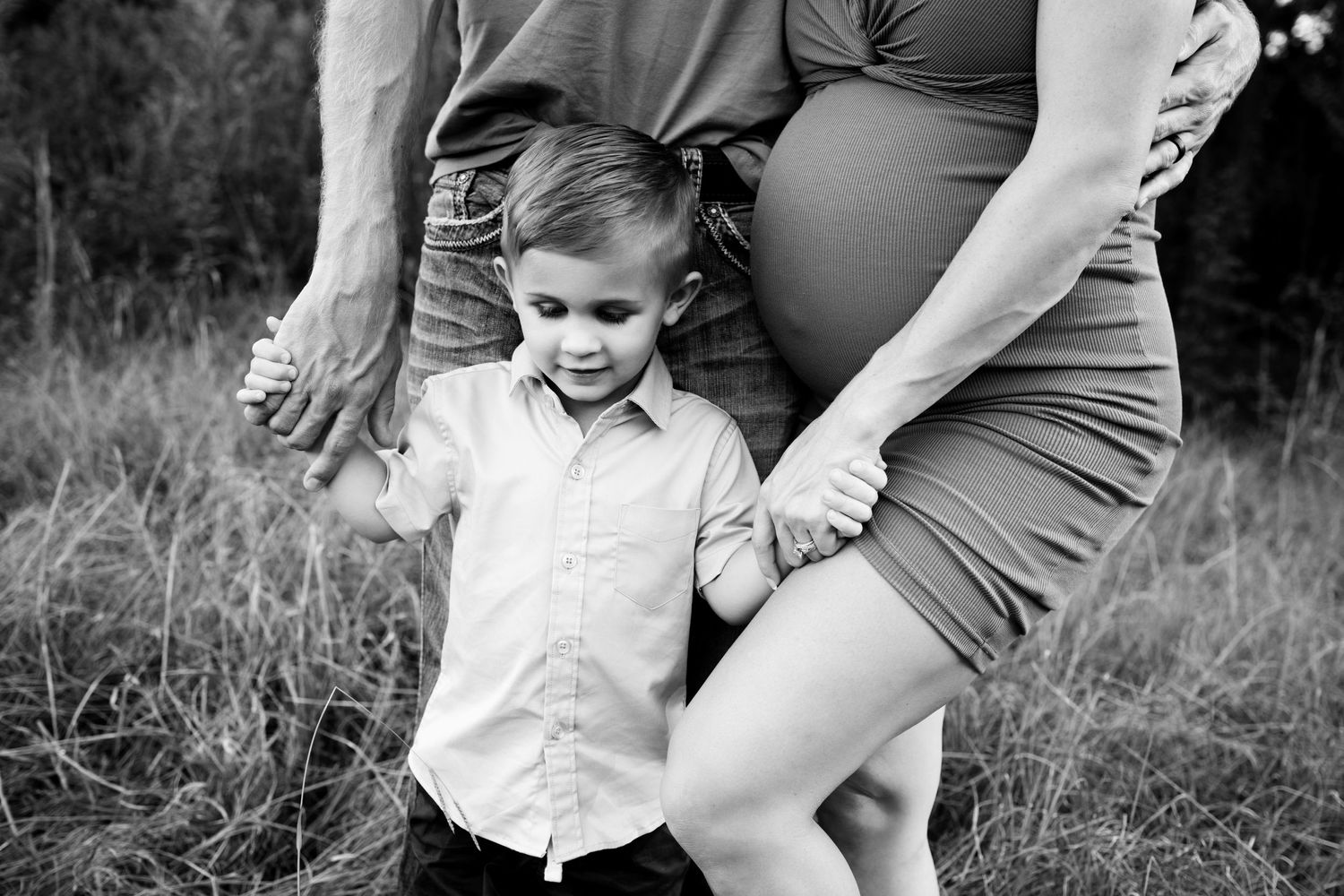 Black and white image of family close together and soon to be big brother holding mom and dad's hands.