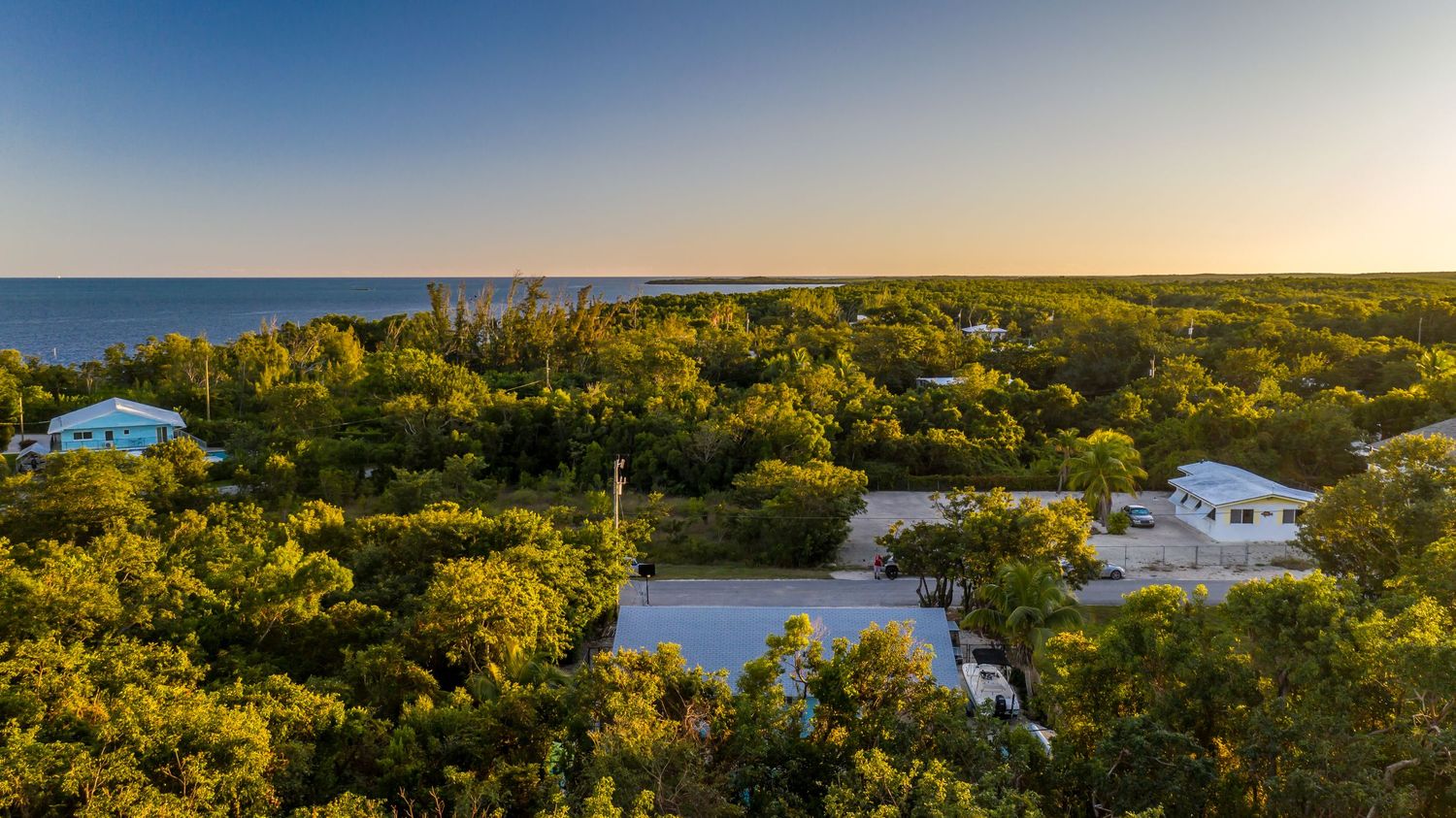 Aerial panoramic view of a coastal community with tropical foliage and waterways at sunset.