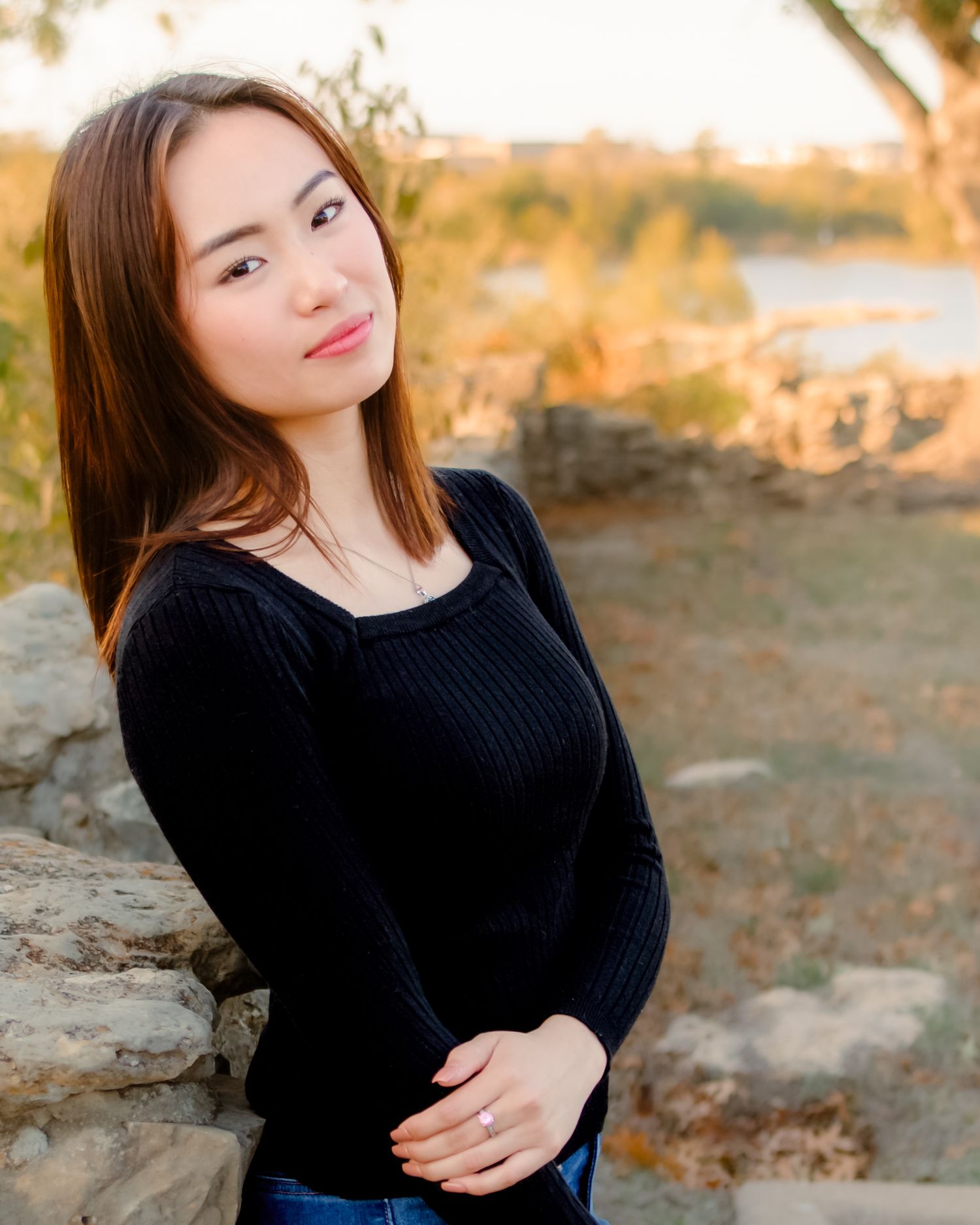 A portrait of a person in a black sweater sitting outdoors during golden hour.