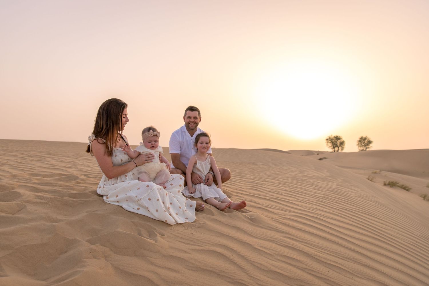 Family sat on dunes at sunset in neutral coloured clothes
