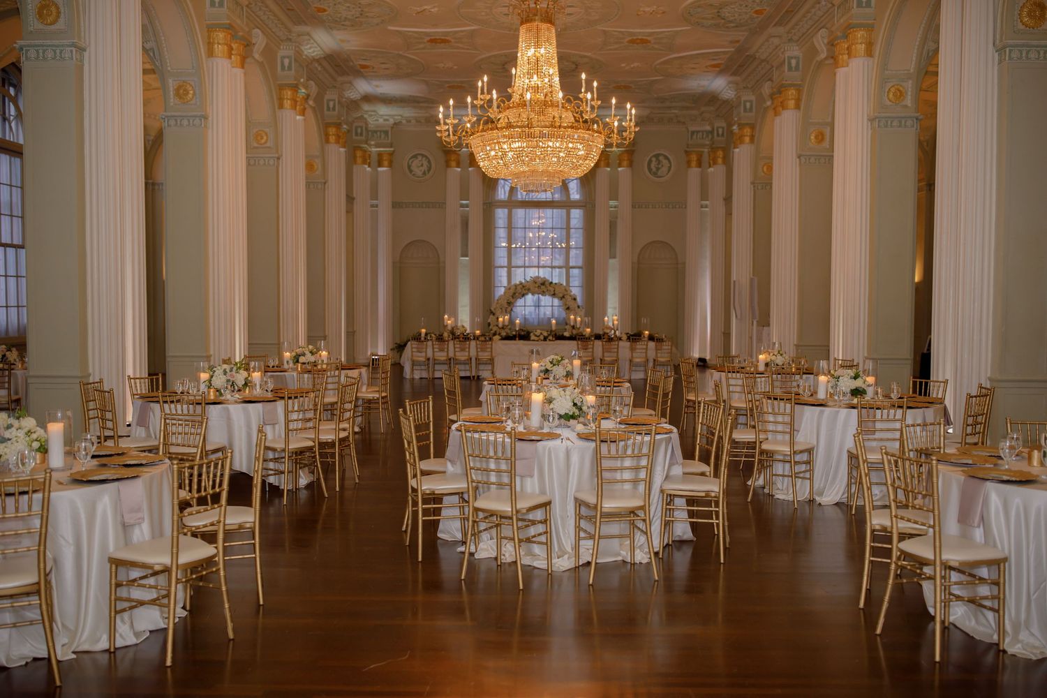 Elegant ballroom set for wedding reception with crystal chandeliers and gold chiavari chairs.