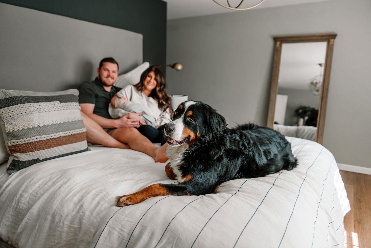 Family relaxing together on white bedding with their black dog.