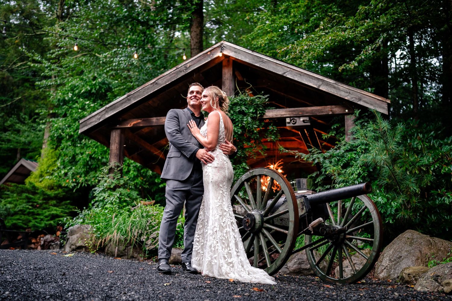 Wedding couple poses in front of rustic wooden structures and vintage wagon wheels outdoors.