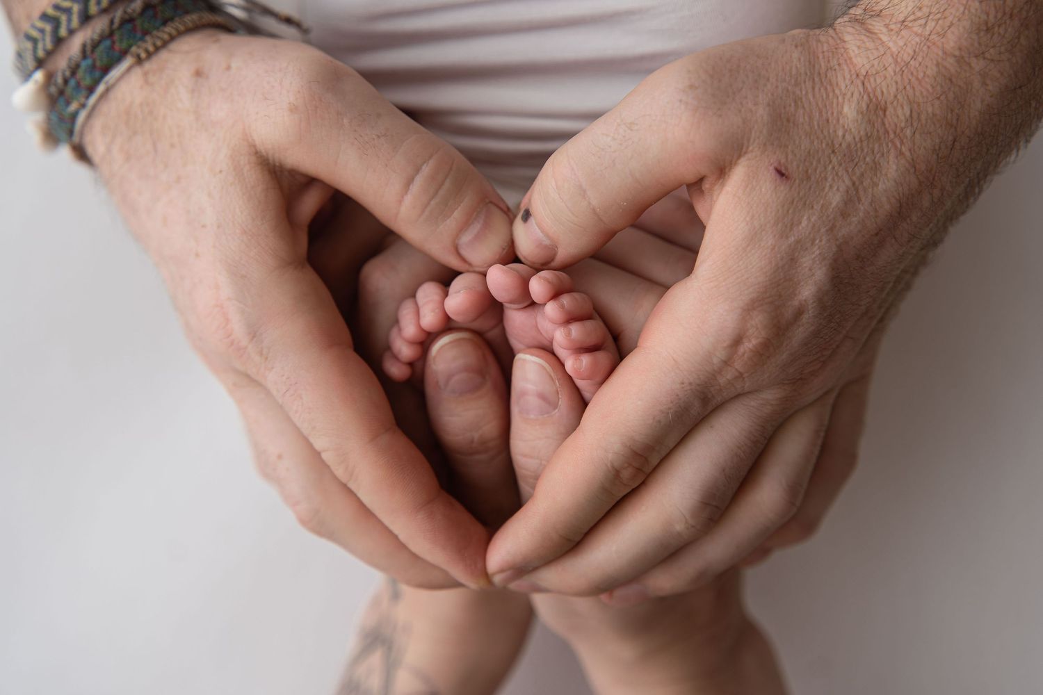 Close-up of adult hands gently cradling tiny newborn baby feet with a tattoo visible on wrist.