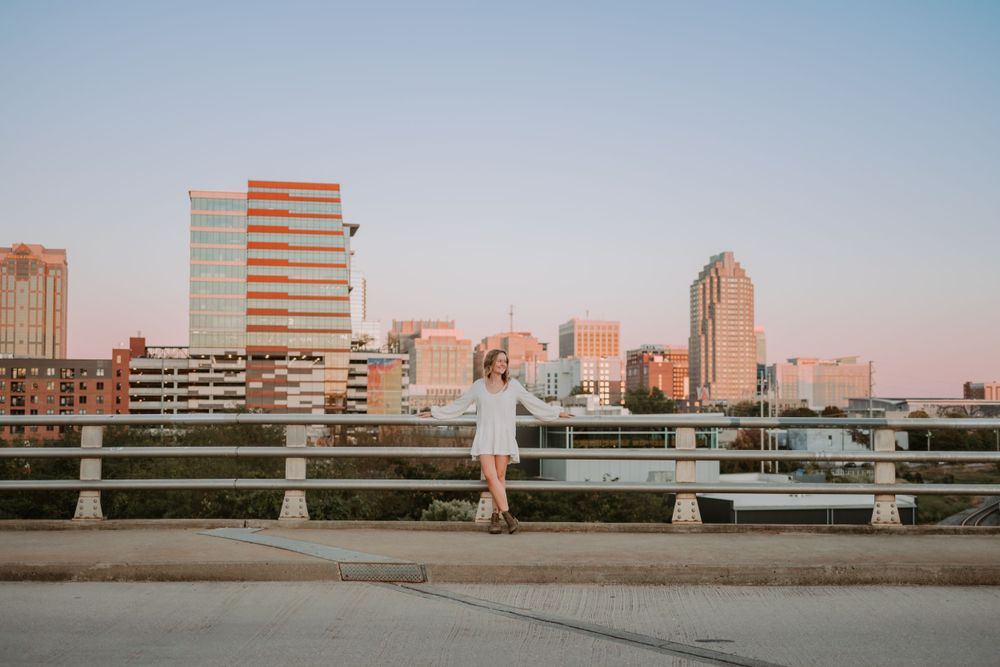 Woman in white dress standing on bridge against urban cityscape at sunset.