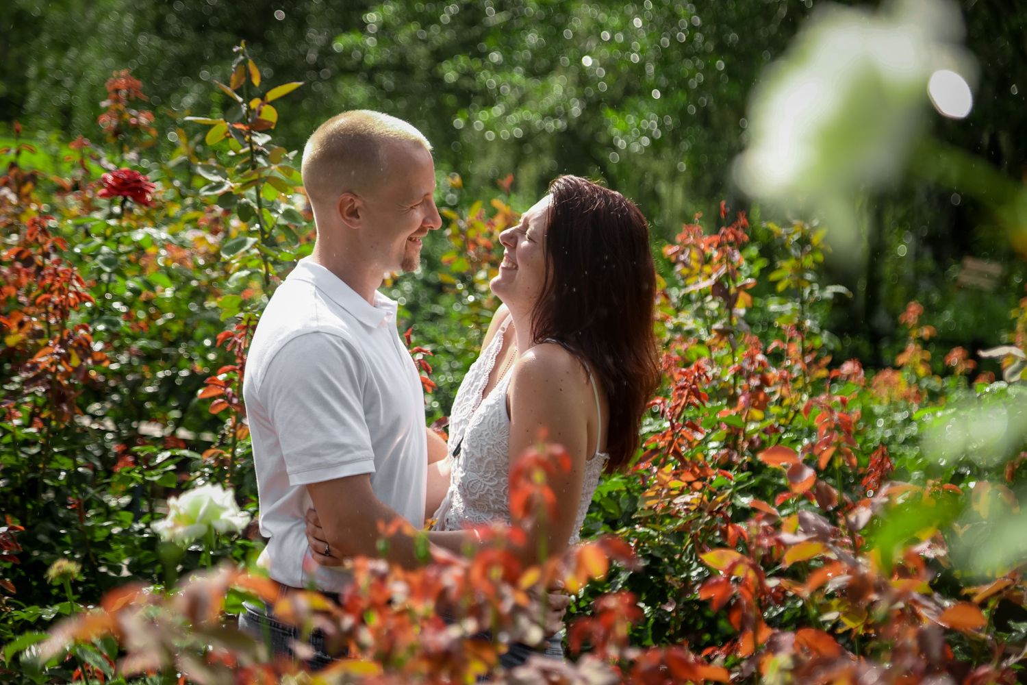 Couple stands close together in blooming garden with orange flowers.