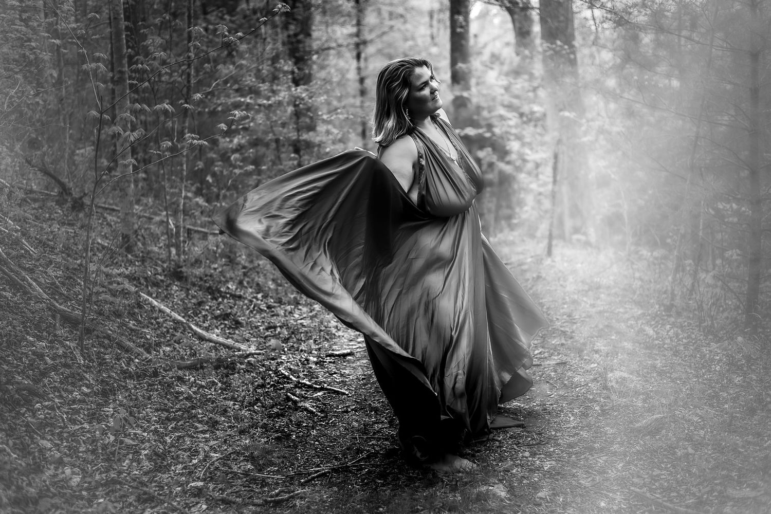 Mysterious figure in flowing dress twirls through misty forest in black and white.