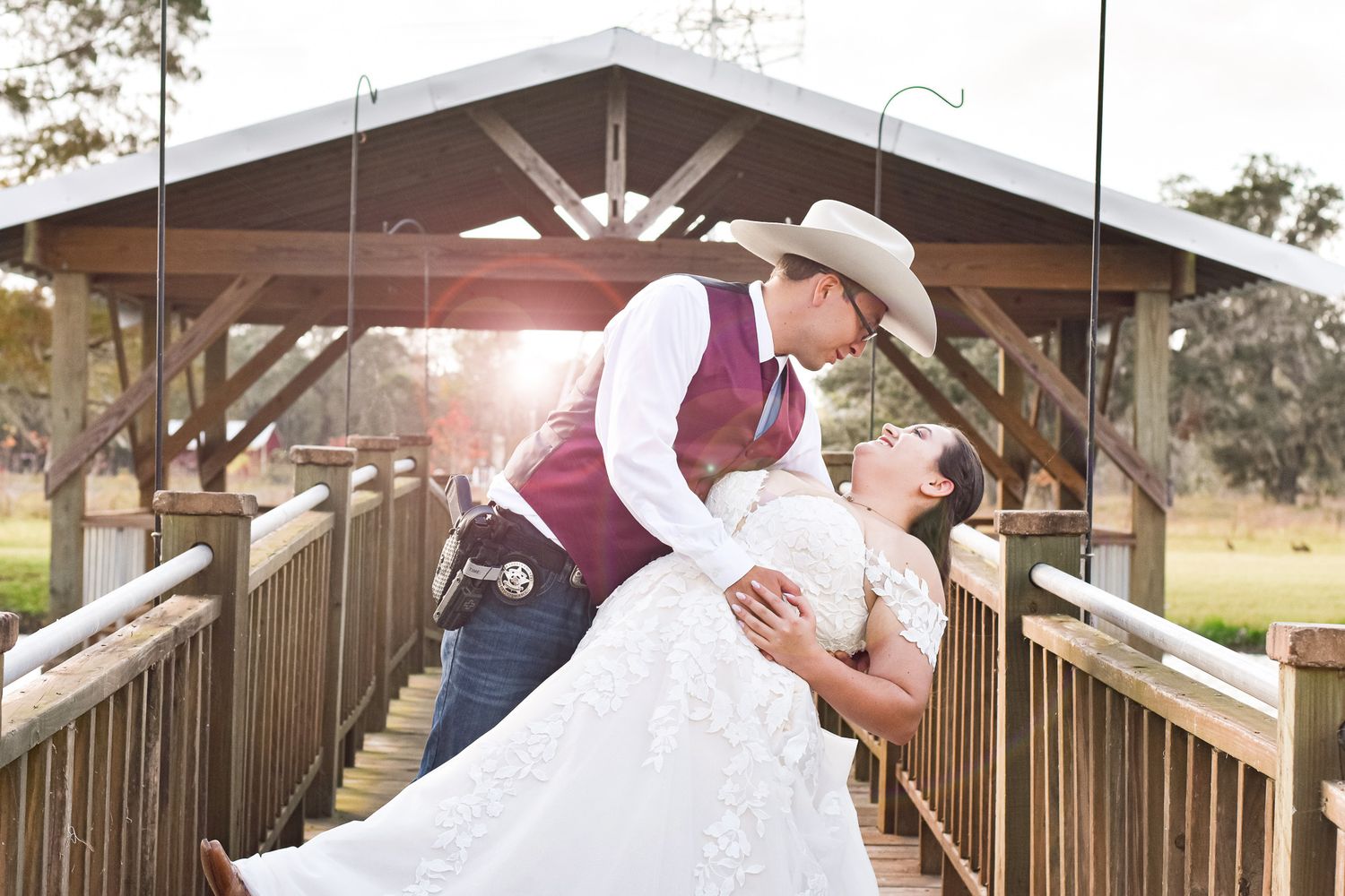 A romantic wedding photo of a couple in western attire sharing an intimate moment on a covered wooden bridge.