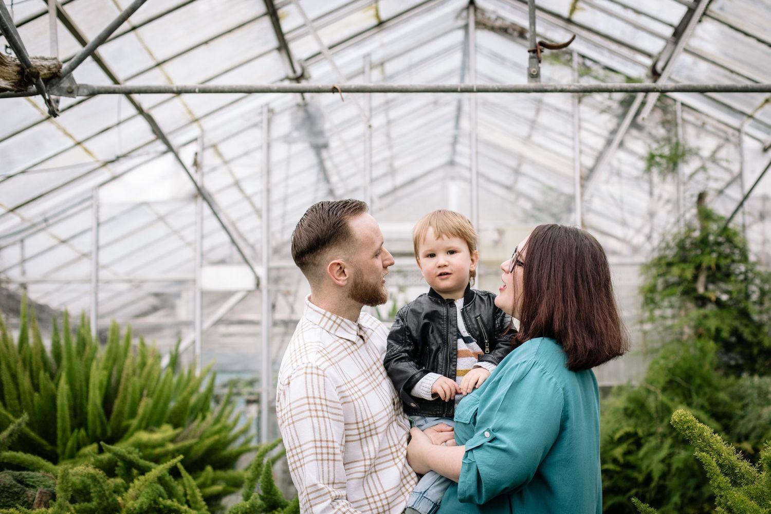 Family enjoying time together in a greenhouse filled with lush ferns and plants.