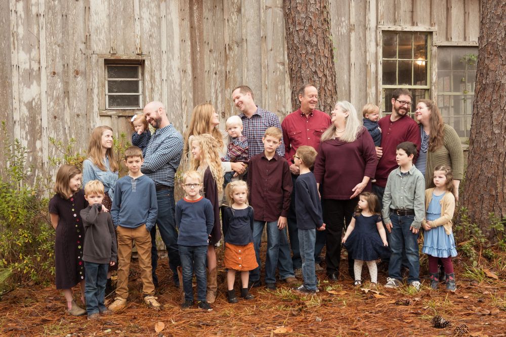 A large family group poses together outside a rustic wooden barn on fallen autumn leaves.
