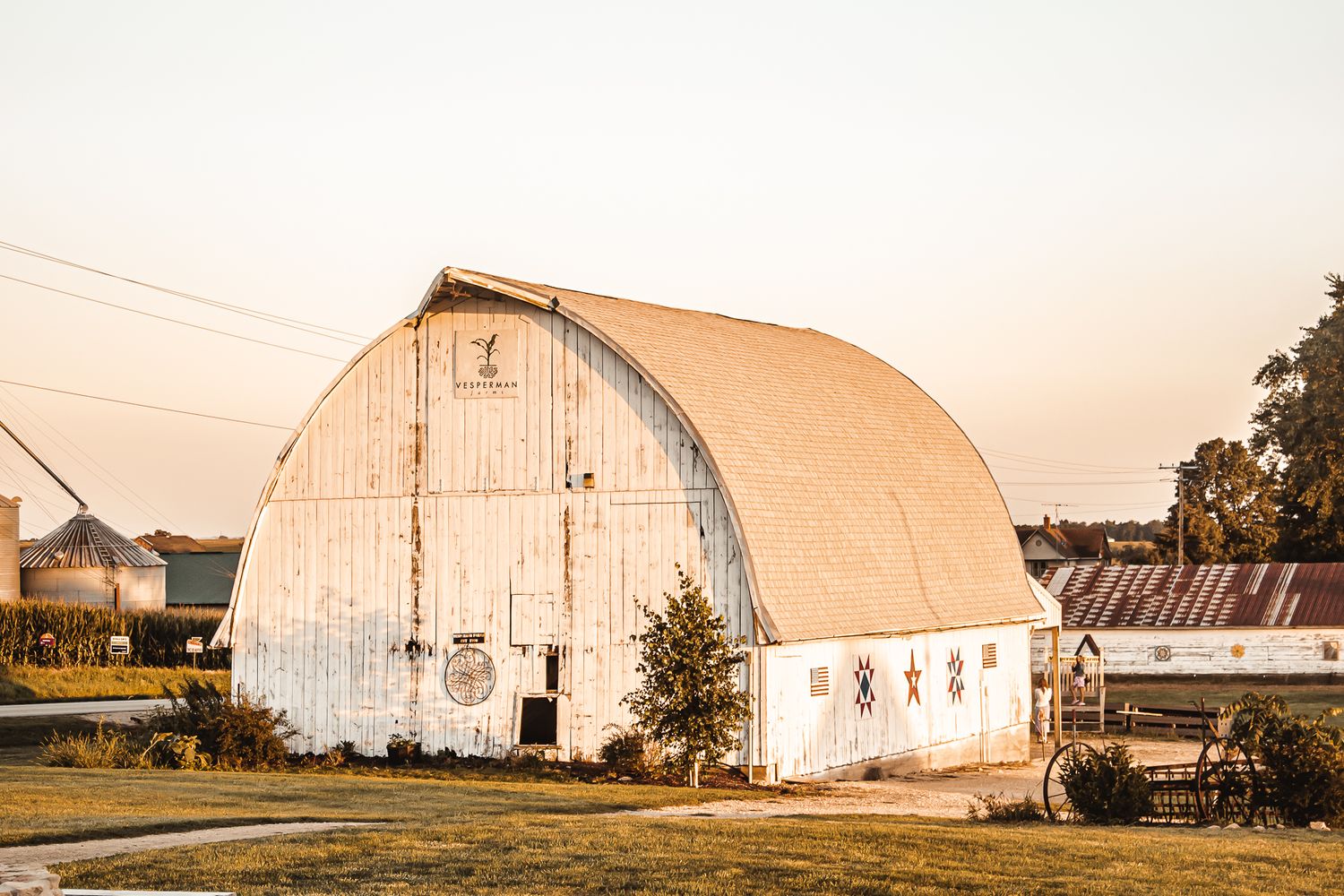 A weathered white barn with an arched roof glows warmly in the sunset light.