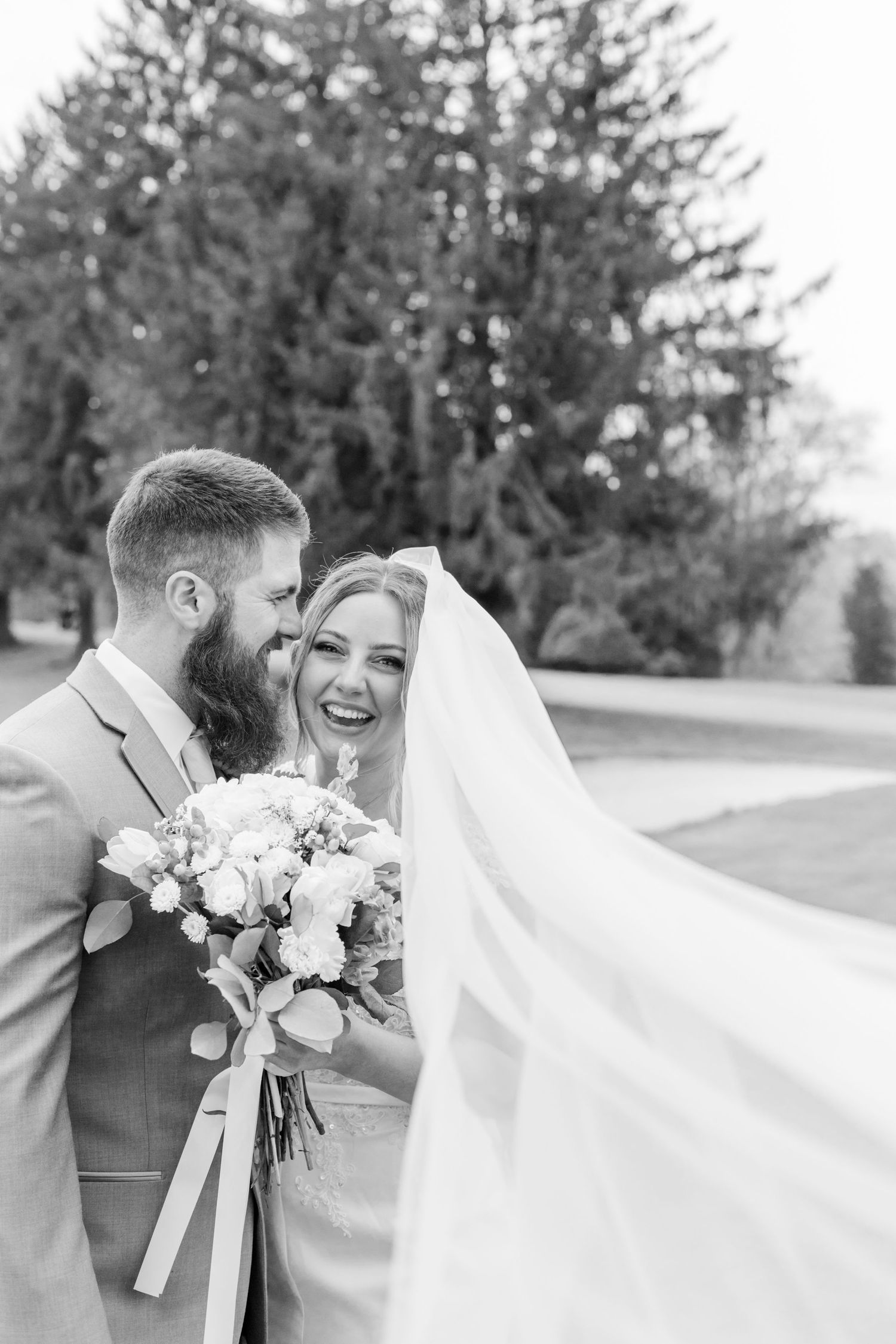 Romantic outdoor wedding portrait with flowing veil and white floral bouquet.