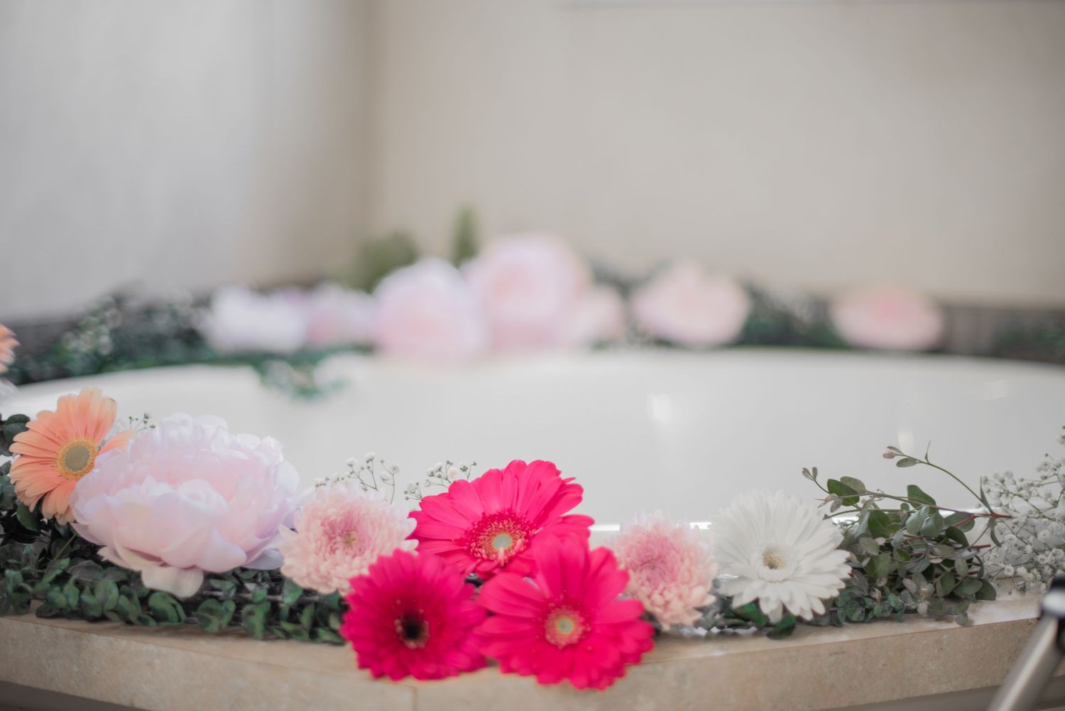 Pink and white flowers arranged with greenery along the edge of a white bathtub.