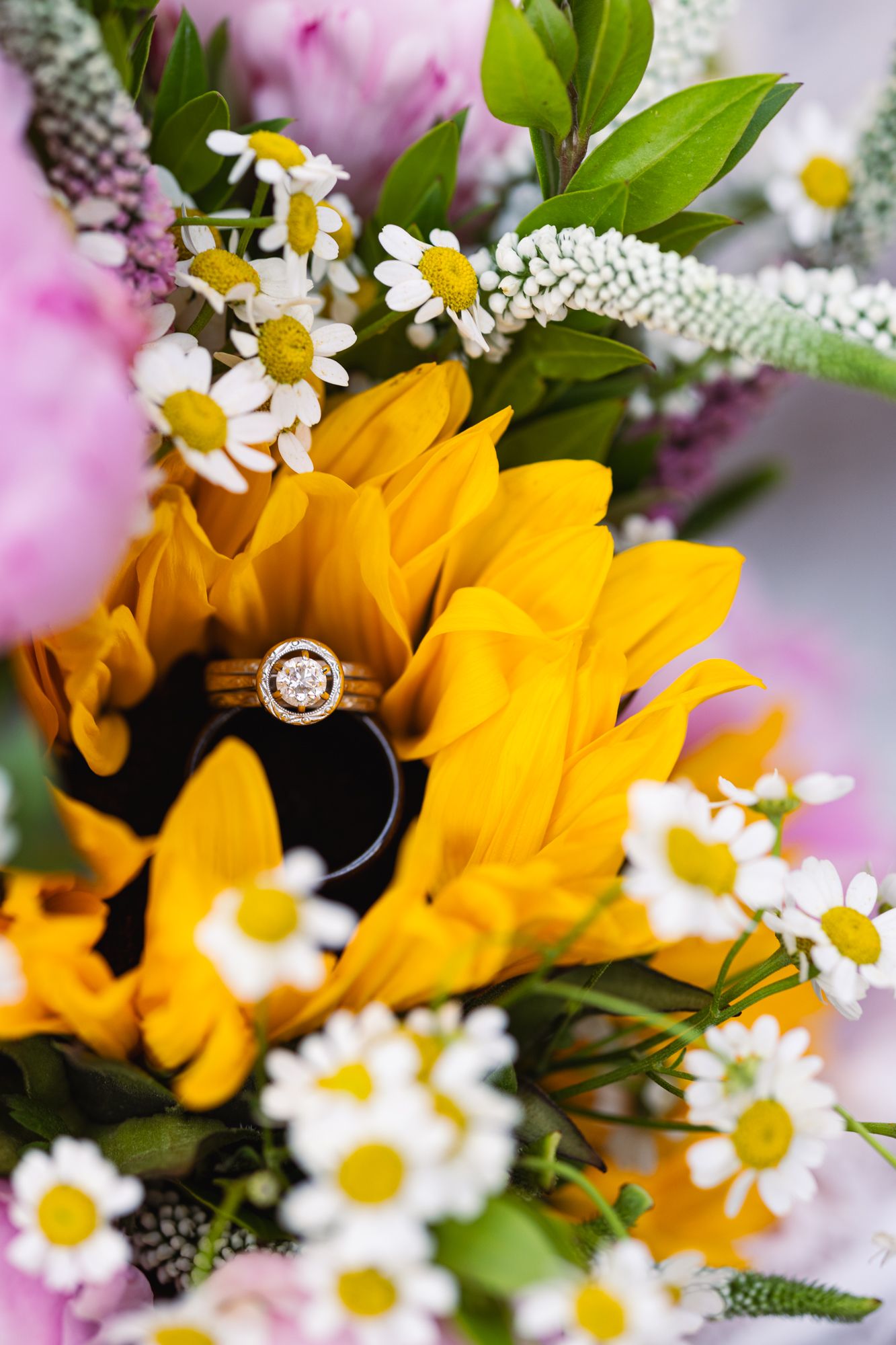 An engagement ring nestled in a bouquet of sunflowers and daisies.