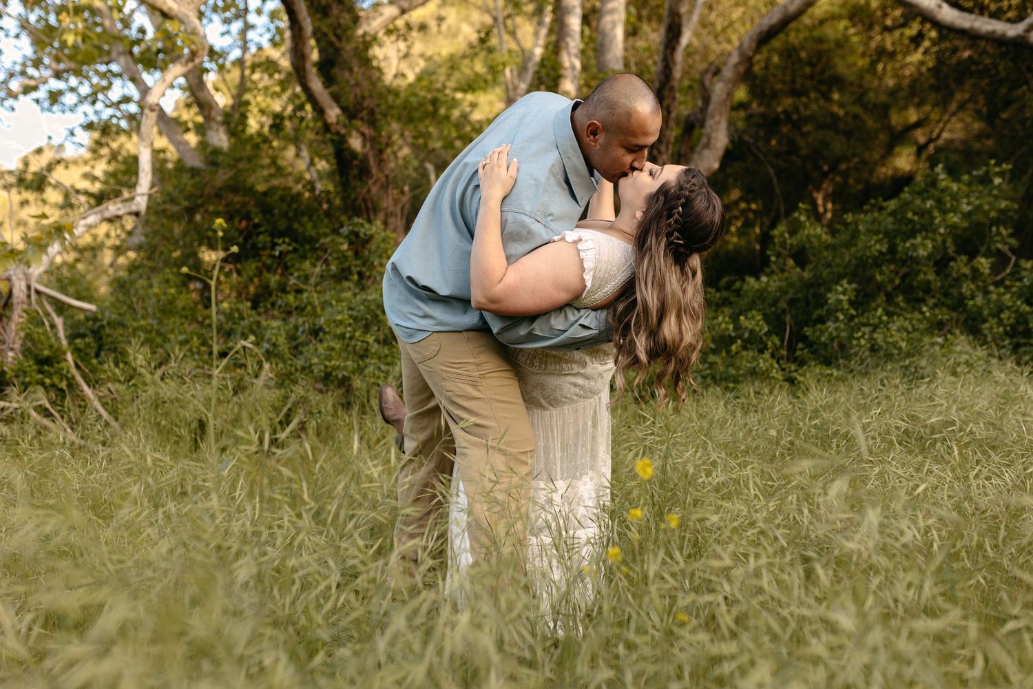 Romantic outdoor couple photo session in golden sunlight among trees and tall grass.