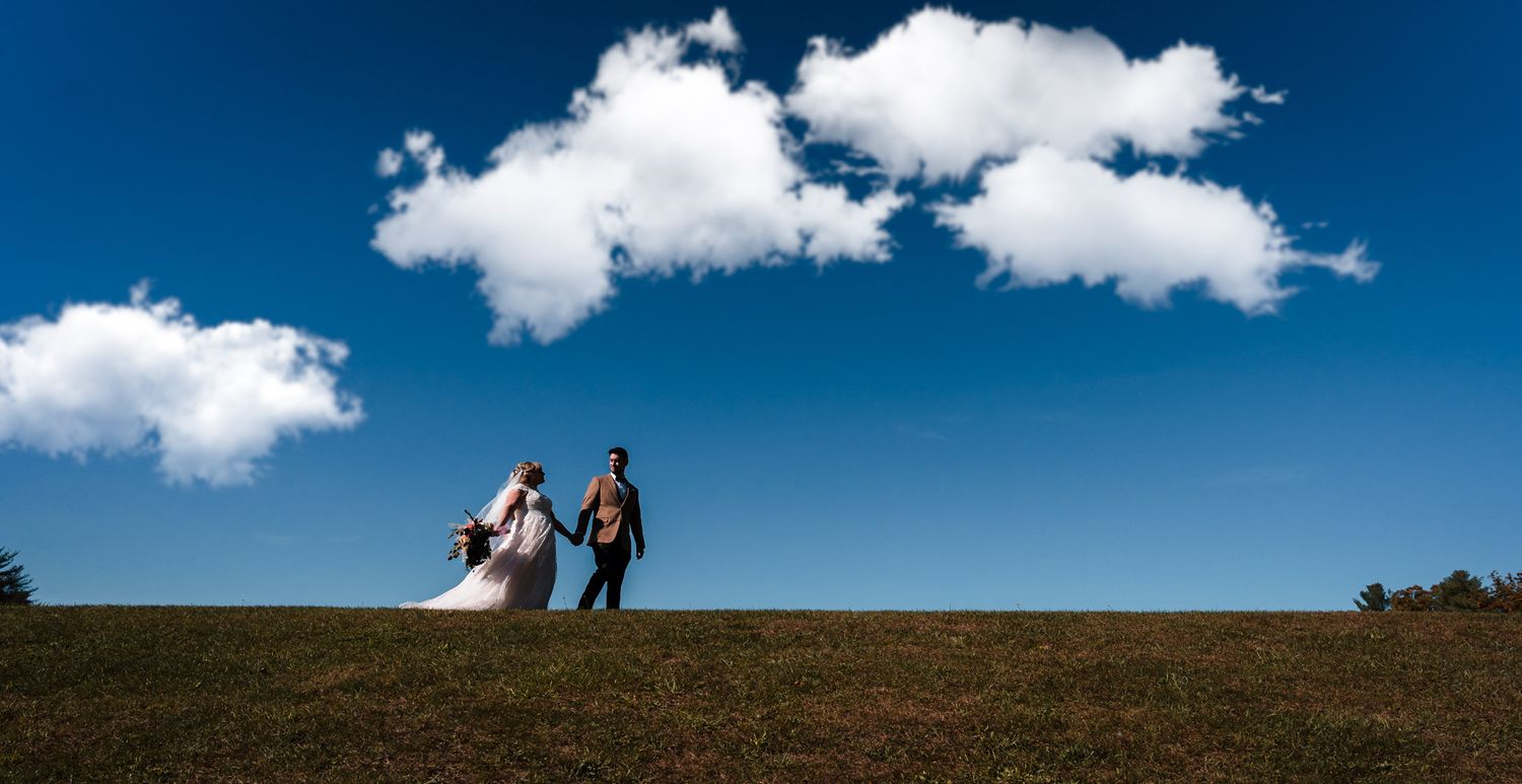 Silhouettes walking on hilltop against bright blue sky with scattered clouds.