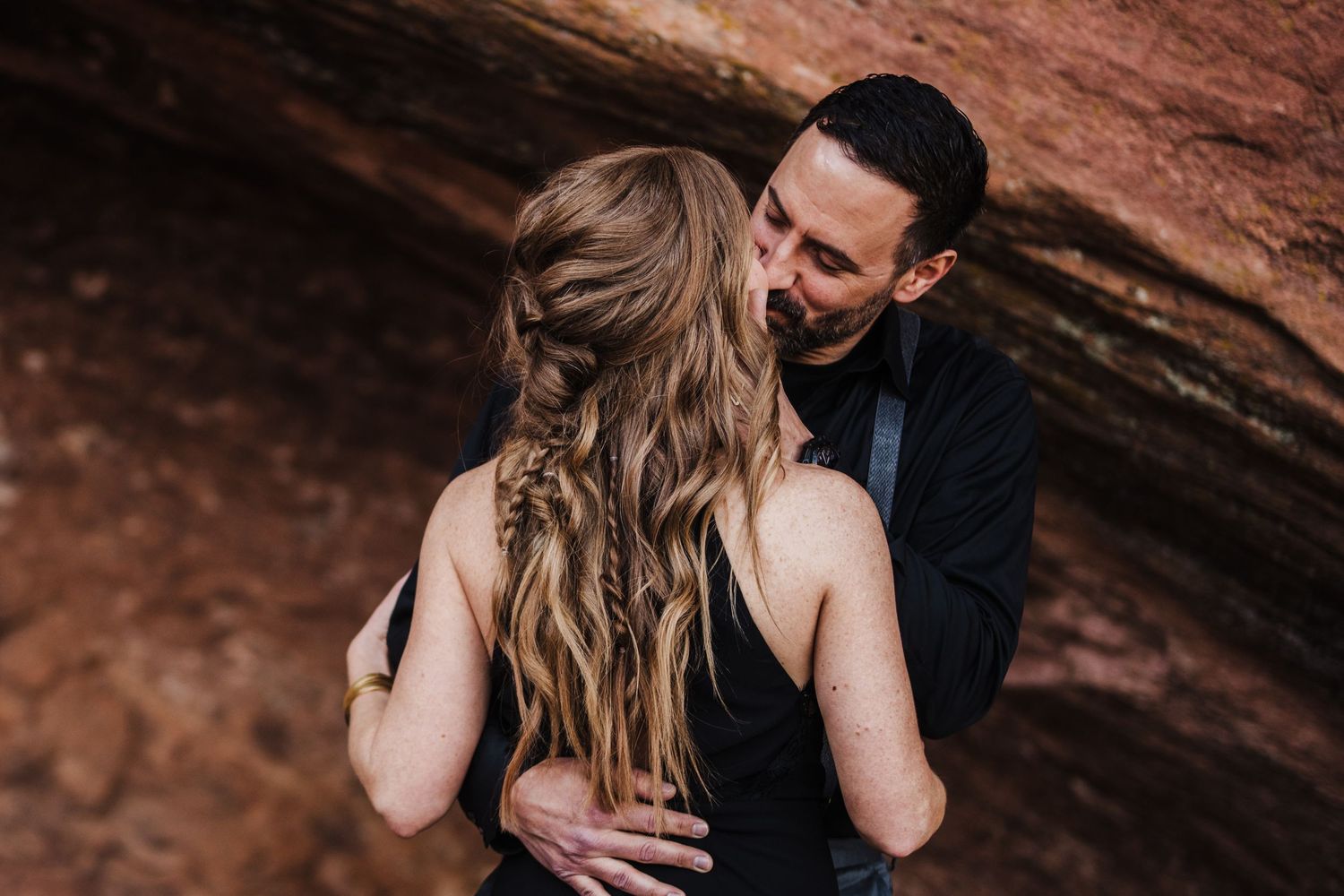 Couple shares intimate moment against red rock backdrop during sunset photoshoot.