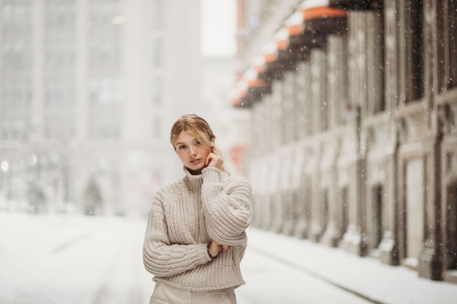 Person in cozy beige sweater standing in snowy urban setting.