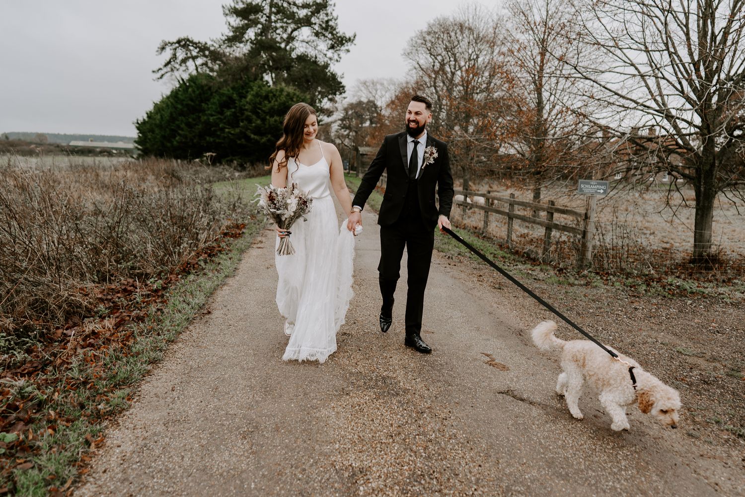 a bride and groom walking along a country lane with their dog.