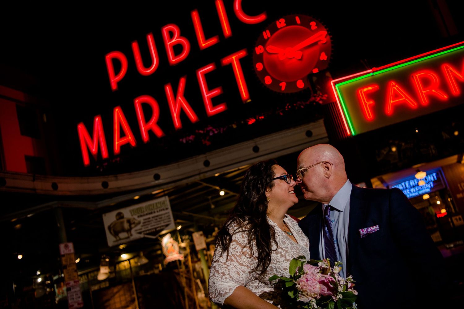 A romantic nighttime portrait beneath the glowing red Public Market sign.