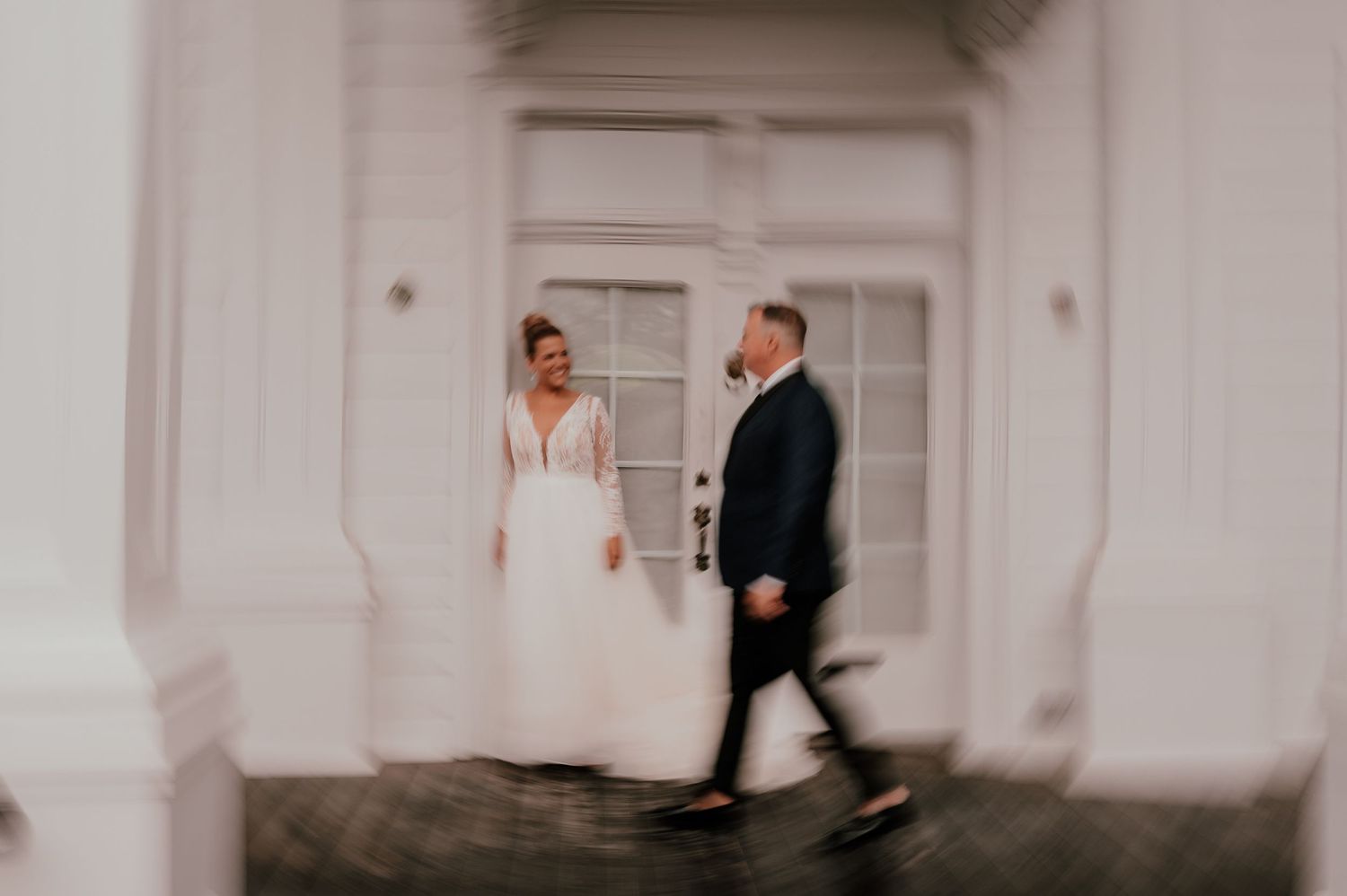 Elegant wedding couple walking through a doorway in a white corridor.